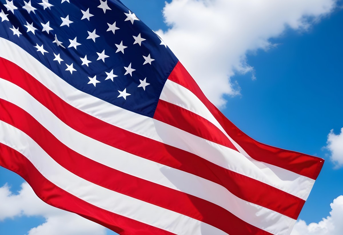 American Flag Waving In The Wind With Its Red And White Stripes And Blue Field Of Stars Against A Blue Sky With White Clouds 7 B440