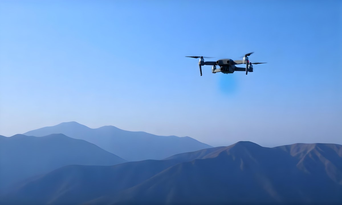 A Blue Drone Flying Over The Mountains With Mountains In The Background And A Clear Blue Sky 11 558f
