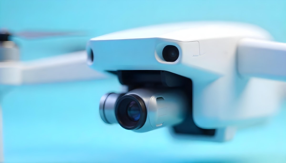 A Close Up Of A Drone Camera With A Lens And Blue Body Mounted On A White Drone With A Light Blue Background 19 31ba