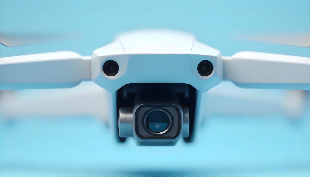 A Close Up Of A Drone Camera With A Lens And Blue Body Mounted On A White Drone With A Light Blue Background 3 25a0