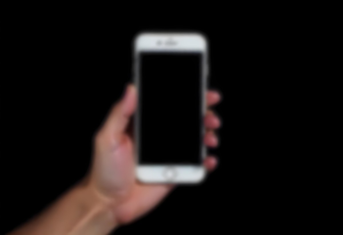 A Fair Skinned Hand Holding A White Smartphone With A Blank Black Screen Isolated On A Black Background 9 66a8