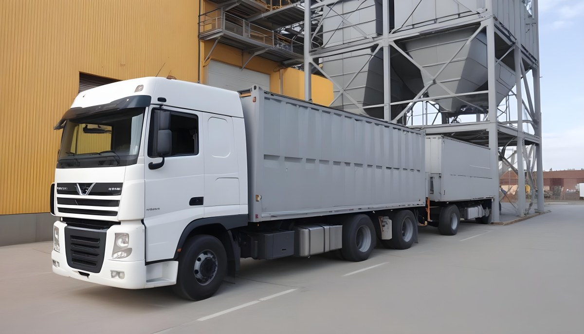 A Yellow Truck With A White Container Parked In Front Of A Factory With Metal Structures And Gray Walls 3 B72e