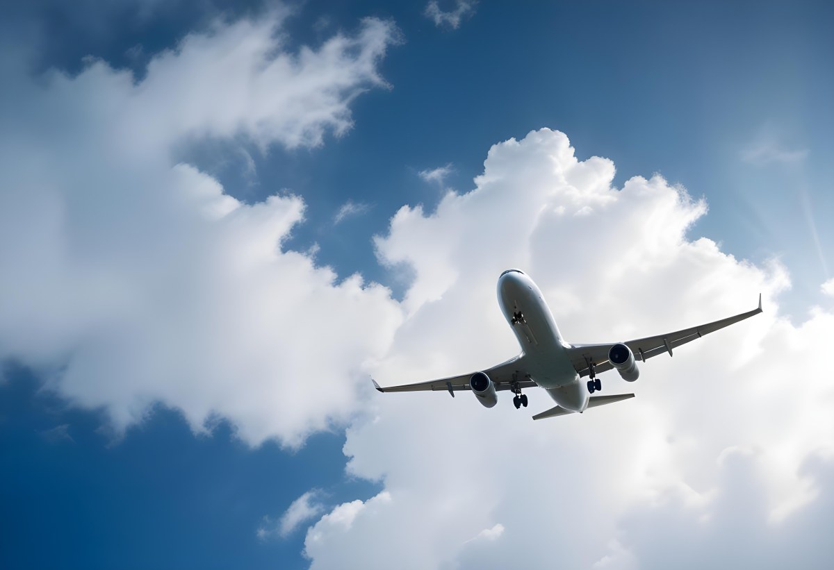 An Airplane Flying Against A Backdrop Of Blue Sky With Scattered Clouds The Aircraft Is Viewed From Below Showcasing Its Wings And Tail 11 2e77