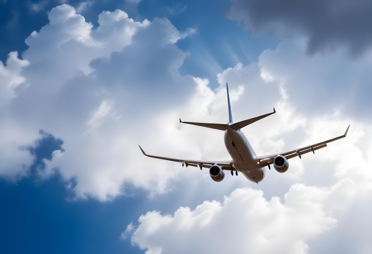 An Airplane Flying Against A Backdrop Of Blue Sky With Scattered Clouds The Aircraft Is Viewed From Below Showcasing Its Wings And Tail 14 48be