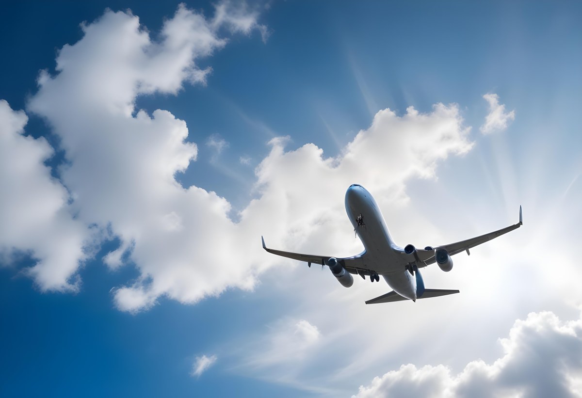 An Airplane Flying Against A Backdrop Of Blue Sky With Scattered Clouds The Aircraft Is Viewed From Below Showcasing Its Wings And Tail 2 Cb03