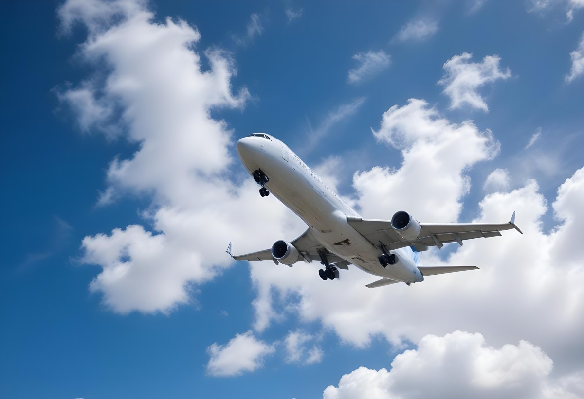 An Airplane Flying Against A Backdrop Of Blue Sky With Scattered Clouds The Aircraft Is Viewed From Below Showcasing Its Wings And Tail 22 9ec8