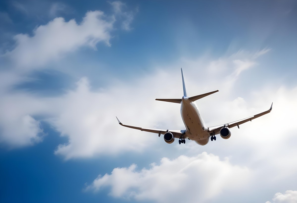 An Airplane Flying Against A Backdrop Of Blue Sky With Scattered Clouds The Aircraft Is Viewed From Below Showcasing Its Wings And Tail 4 9f4d