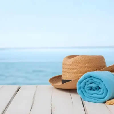 A Straw Hat And A White Towel On A White Wooden Table With A Blurred Background Of The Sea And The Sky 19 Af96