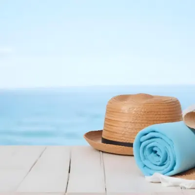 A Straw Hat And A White Towel On A White Wooden Table With A Blurred Background Of The Sea And The Sky 21 5ada