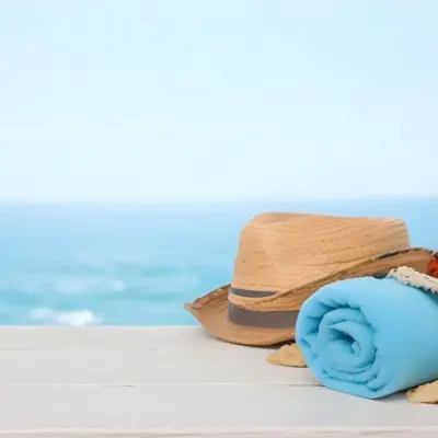 A Straw Hat And A White Towel On A White Wooden Table With A Blurred Background Of The Sea And The Sky 23 3e08