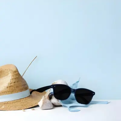A Straw Hat With A Blue Ribbon Black Sunglasses A Seashell And A Seashell On A White Surface With A Light Blue Background 1 A2df