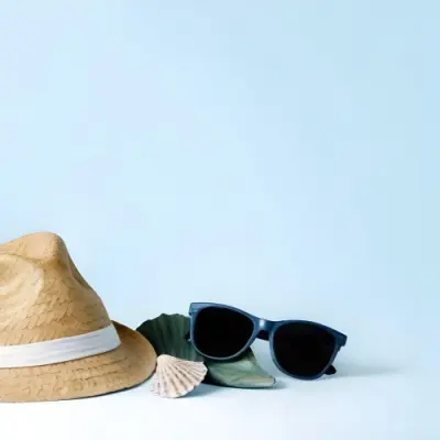 A Straw Hat With A Blue Ribbon Black Sunglasses A Seashell And A Seashell On A White Surface With A Light Blue Background 13 13c9