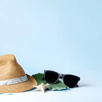 A Straw Hat With A Blue Ribbon Black Sunglasses A Seashell And A Seashell On A White Surface With A Light Blue Background 5 914e