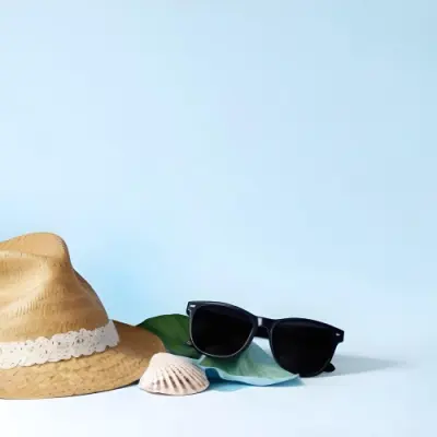A Straw Hat With A Blue Ribbon Black Sunglasses A Seashell And A Seashell On A White Surface With A Light Blue Background 7 4c5c