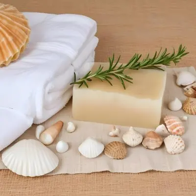 A Bar Of Soap Placed On A Woven Mat Surrounded By Various Seashells And A Sprig Of Rosemary In The Background There Are Neatly Stacked White Towels And A Natural Sponge The Setting Has A Calming Spa Like Atmospher 12 Bbf1