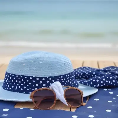 A Blue Hat With A White Ribbon Sunglasses And A White Scarf With Blue Dots On A Wooden Surface Beach In The Background 18