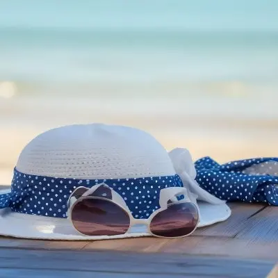A Blue Hat With A White Ribbon Sunglasses And A White Scarf With Blue Dots On A Wooden Surface Beach In The Background 2 60b6