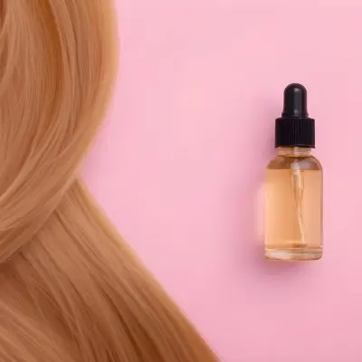 A Bottle Of Hair Oil And A Strand Of Blonde Hair On A Pink Background 2 955b