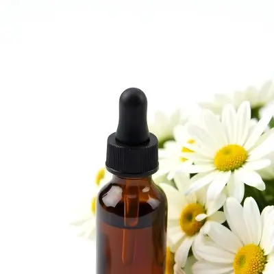 A Bottle Of Yellow Liquid Surrounded By White Daisy Flowers On A Light Background 17 C89c