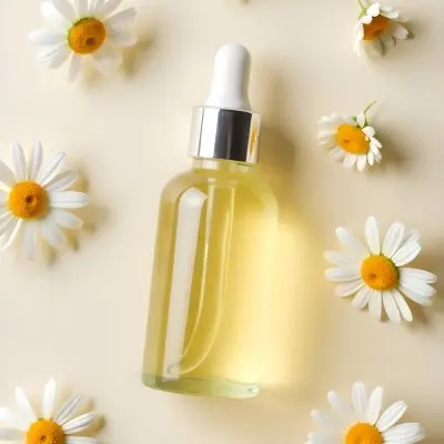 A Bottle Of Yellow Liquid Surrounded By White Daisy Flowers On A Light Background 24 C43d