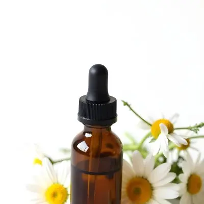 A Bottle Of Yellow Liquid Surrounded By White Daisy Flowers On A Light Background 29 Be7c