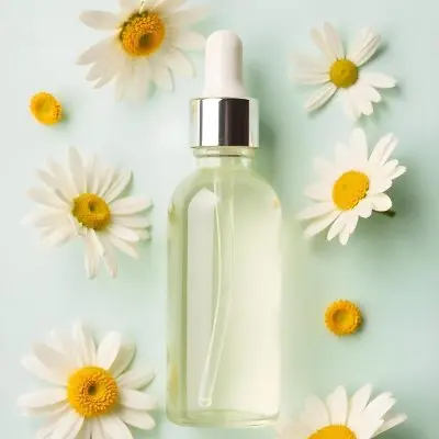 A Bottle Of Yellow Liquid Surrounded By White Daisy Flowers On A Light Background 5 9079
