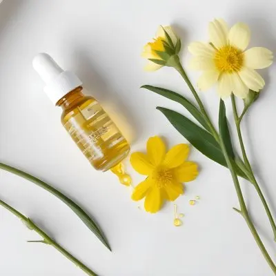 A Bottle Of Yellow Oil With A Dropper Next To Some Yellow Flowers On A White Surface 22 65cd