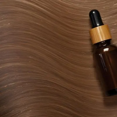 A Brown Glass Bottle With A Dropper On A Background Of Brown Hair The Hair Is Wavy And Shiny The Bottle Is In The Upper Right Corner 9