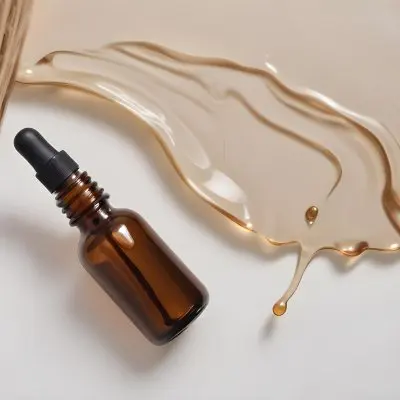 A Brown Glass Bottle With A Dropper On A White Surface With Brown Wavy Hair In The Background 10 9e85