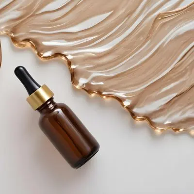 A Brown Glass Bottle With A Dropper On A White Surface With Brown Wavy Hair In The Background 11 C8d7