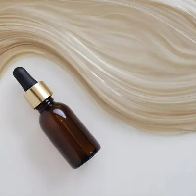 A Brown Glass Bottle With A Dropper On A White Surface With Brown Wavy Hair In The Background 13 8566