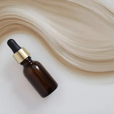 A Brown Glass Bottle With A Dropper On A White Surface With Brown Wavy Hair In The Background 17 5d54