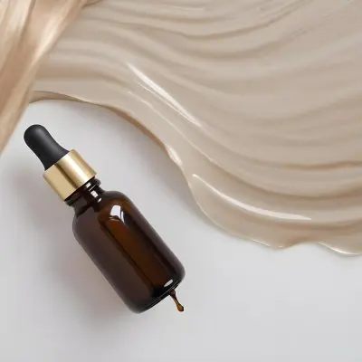 A Brown Glass Bottle With A Dropper On A White Surface With Brown Wavy Hair In The Background 19 9d69