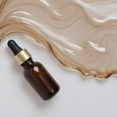 A Brown Glass Bottle With A Dropper On A White Surface With Brown Wavy Hair In The Background 28 7e87