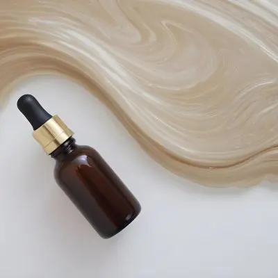 A Brown Glass Bottle With A Dropper On A White Surface With Brown Wavy Hair In The Background 40 C73e