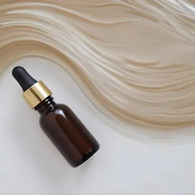 A Brown Glass Bottle With A Dropper On A White Surface With Brown Wavy Hair In The Background 8 4ff6