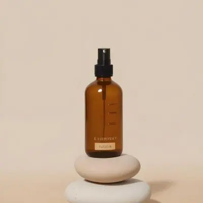 A Brown Glass Spray Bottle With A Black Nozzle Labeled Everyday Oil Is Positioned On Top Of Three Smooth Stacked Stones The Background Is A Soft Beige Color Creating A Minimalist Aesthetic 33 A4ed