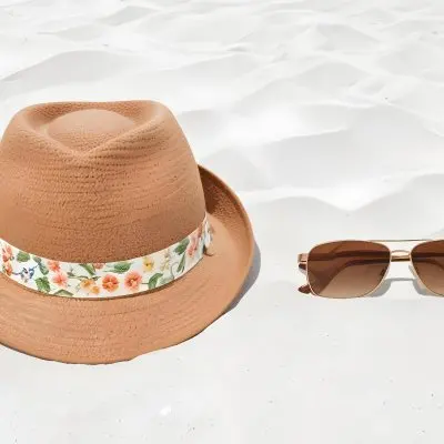 A Brown Hat With A Floral Band And Brown Sunglasses On White Sand 34