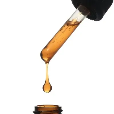 A Close Up Of A Dropper Filled With Amber Liquid Poised Above A Brown Glass Bottle Against A Stark White Background 24 76af