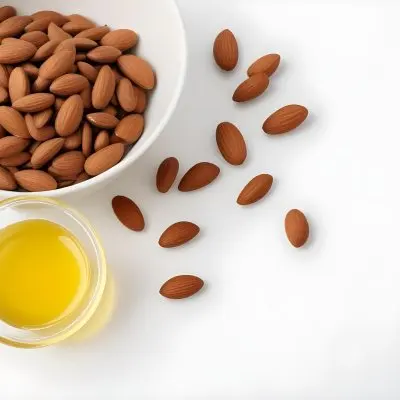 A Close Up Of Brown Hair Strands A Bowl Of Yellow Liquid And Some Almonds On A White Background 29 77c8