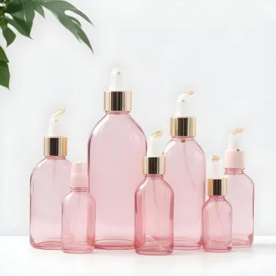 A Collection Of Pink Glass Cosmetic Bottles And Jars With Gold Caps Surrounded By Green Leaves On A White Background 13