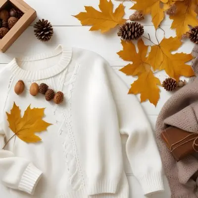 A Flat Lay Arrangement Featuring A Cozy White Knitted Sweater A Brown Knitted Item And A Yellow Hanger Surrounding The Clothing Are Autumn Leaves Pine Cones And A Small Wooden Box Filled With Acorns A Fluffy Orna 14 2e59
