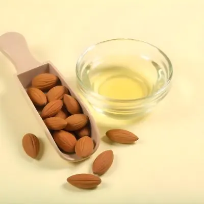 A Glass Jar Filled With Golden Colored Oil Surrounded By Several Whole Almonds On A Light Background 17 A02f