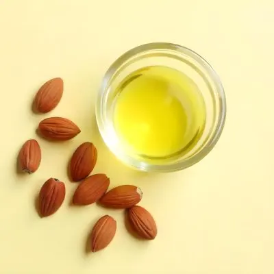 A Glass Jar Filled With Golden Colored Oil Surrounded By Several Whole Almonds On A Light Background 5 B5f3