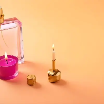 A Golden Perfume Bottle With A Pink Cap And A Golden Candle Holder On A Pink Background 6 2b29