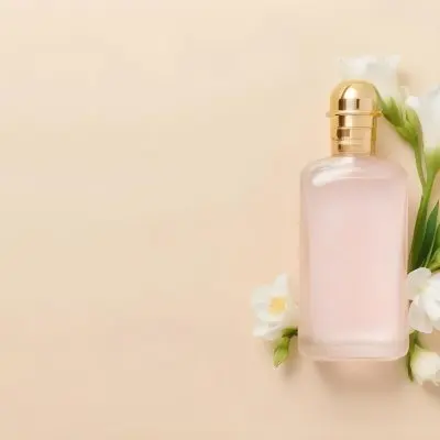 A Golden Perfume Bottle With A Pink Cap Surrounded By White Freesia Flowers All On A White Background 13 7495