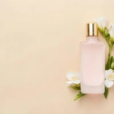 A Golden Perfume Bottle With A Pink Cap Surrounded By White Freesia Flowers All On A White Background 19 790e