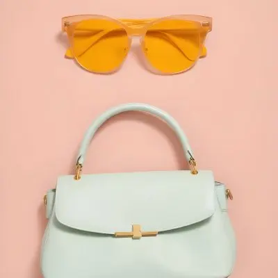 A Mint Green Handbag With A Structured Design Placed On A Light Pink Background Accompanied By A Pair Of Oversized Yellow Sunglasses Positioned Above The Bag 8 7eb9