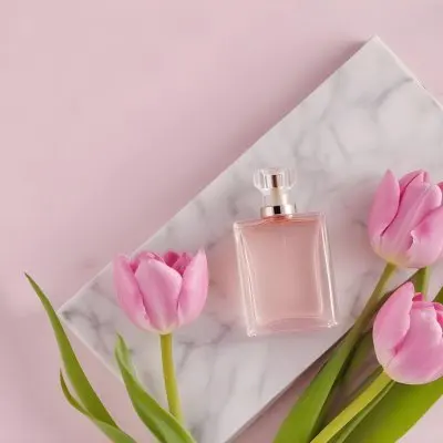 A Perfume Bottle On A Marble Tile Surrounded By Pink Tulips With Green Leaves All Against A Green Background 47 09e5