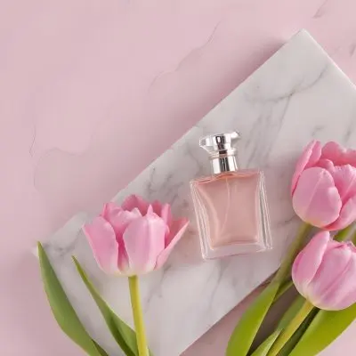 A Perfume Bottle On A Marble Tile Surrounded By Pink Tulips With Green Leaves All Against A Green Background 51 8115